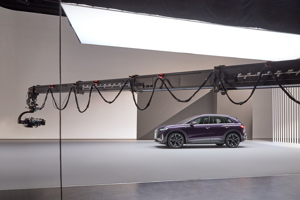 In a film studio, a camera mounted on a pivoting, extendable camera arm is pointed at the Audi Q4 e-tron. 