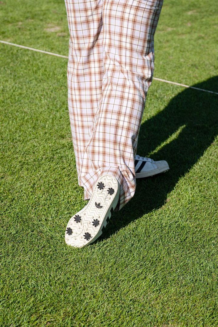 Dettagli dei pantaloni da golf a quadri e delle sneaker che indossa Troy Mullins sul campo da golf. 