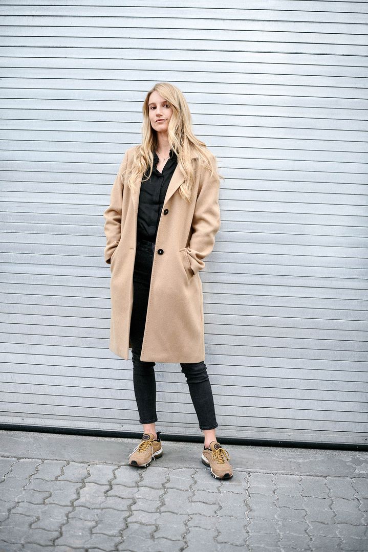 Anna Gasser dans un manteau beige, appuyée contre une porte de garage. 