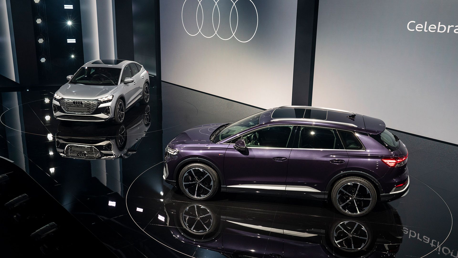 Auf dem Bild sieht man zwei Audi Q4 e-tron Modelle auf der Bühne stehen – silberfarben und lila.