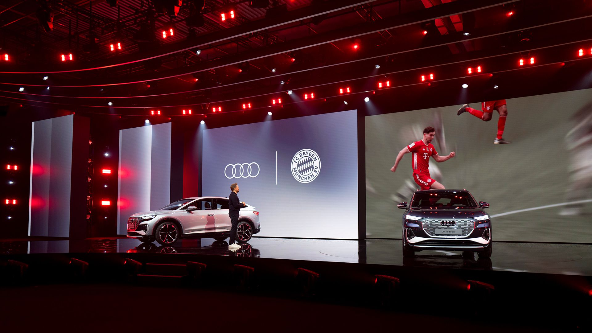 Two Audi models on the stage. The screen is showing soccer players.
