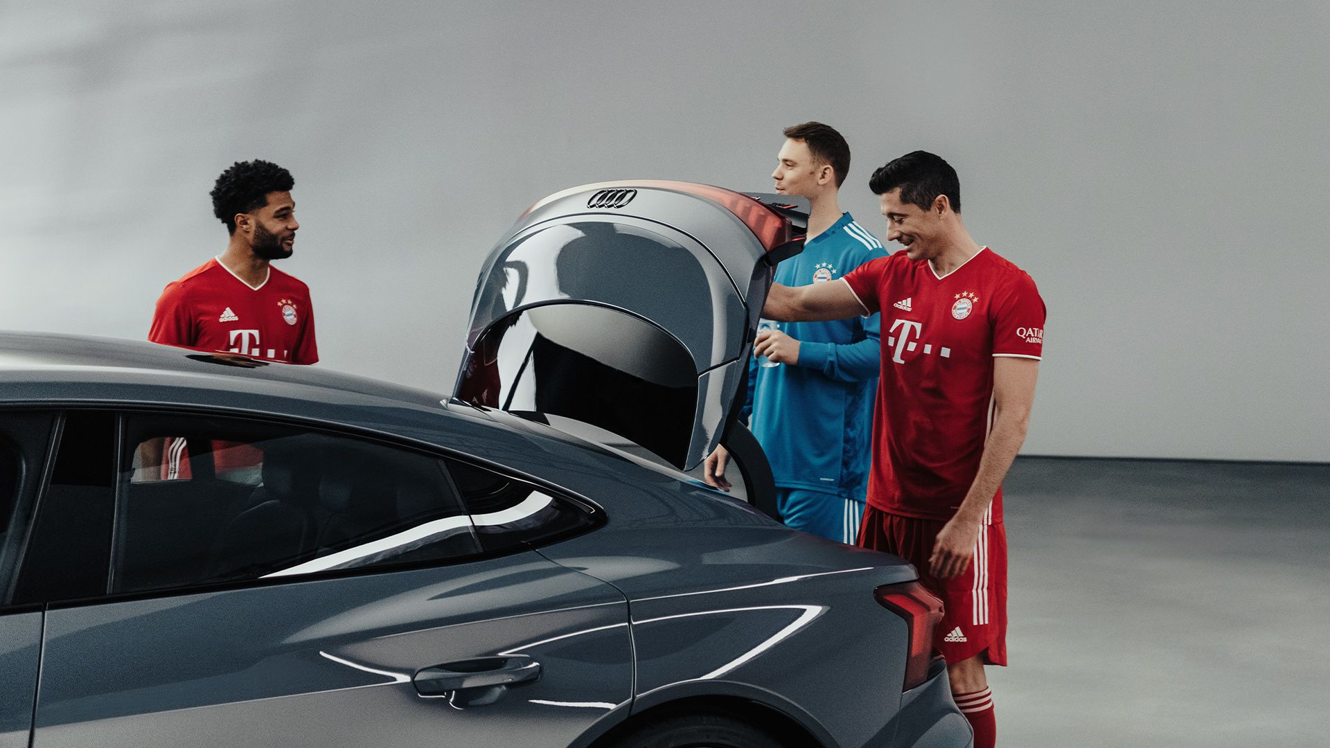 Das Bild zeigt die drei FC-Bayern-Spieler Manuel Neuer, Robert Lewandowski und Serge Gnabry am offenen Kofferraumdeckel des Audi RS e-tron GT. 