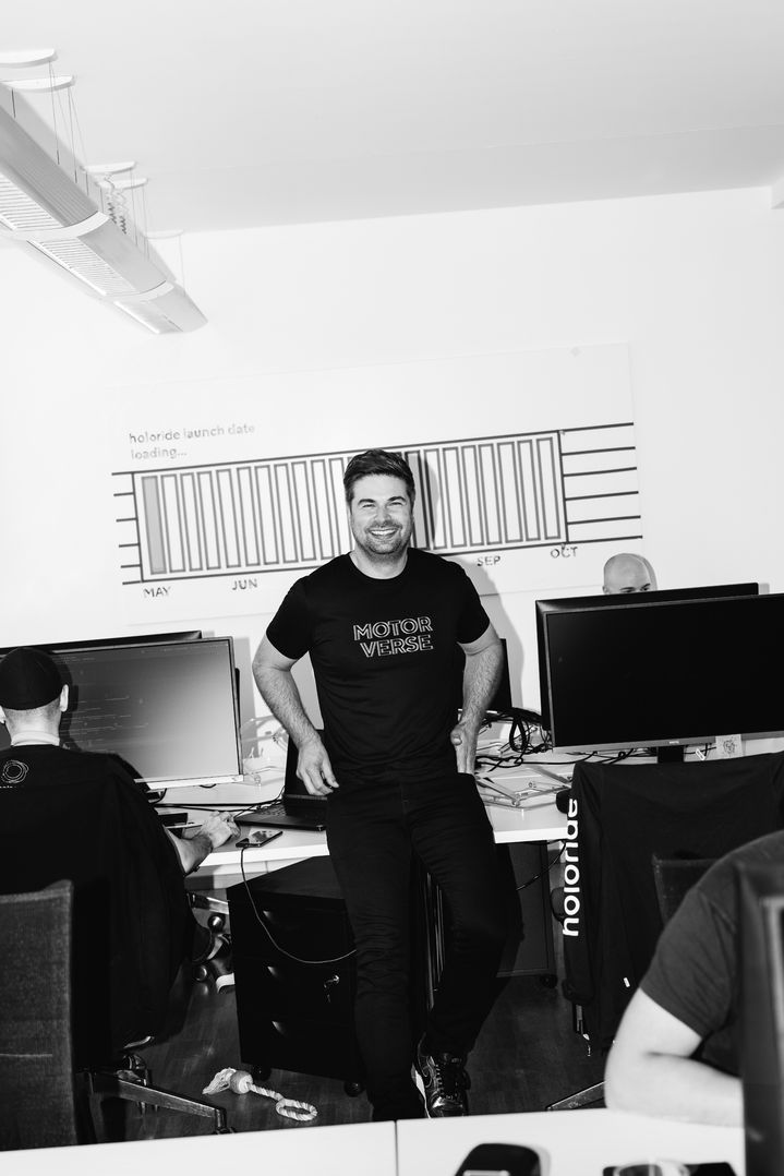 Nils Wollny se tient debout dans son bureau au milieu de son équipe. Son t-shirt porte l’inscription « Motor verse ».