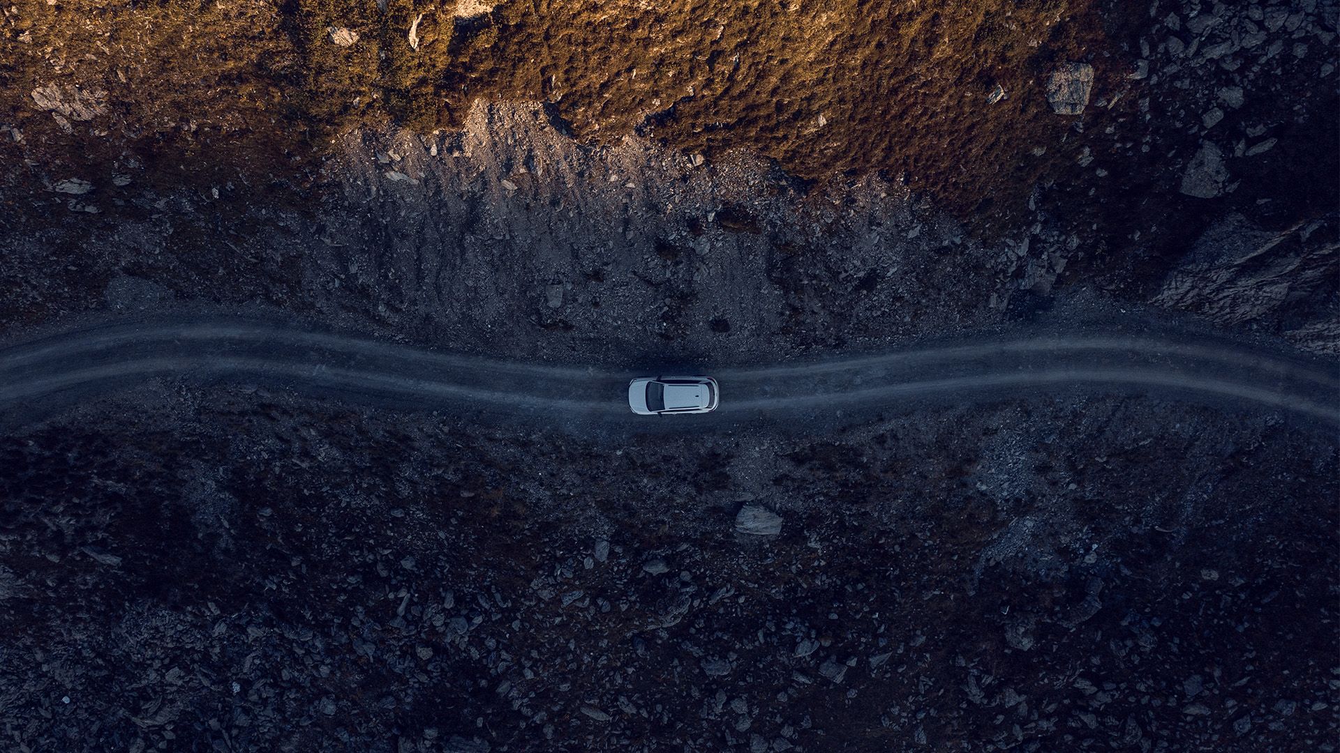 Een dronebeeld van bovenaf toont een witte auto op een weg in de bergen.