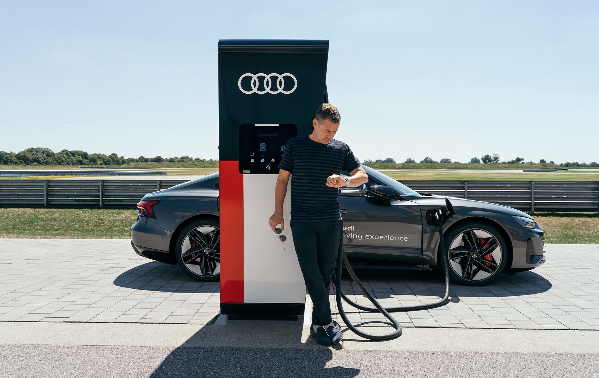 Tom Kristensen leans against an e-charging point while the Audi RS e-tron GT charges.