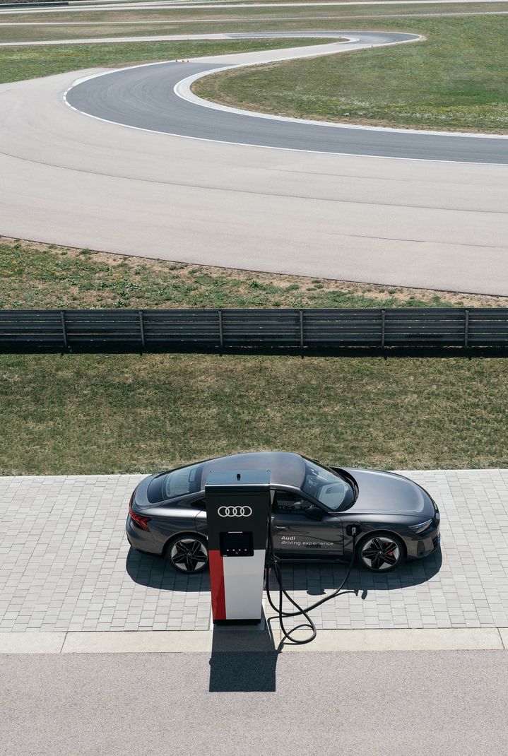 The Audi RS e-tron GT is charging in the foreground, the racetrack can be seen in the background.