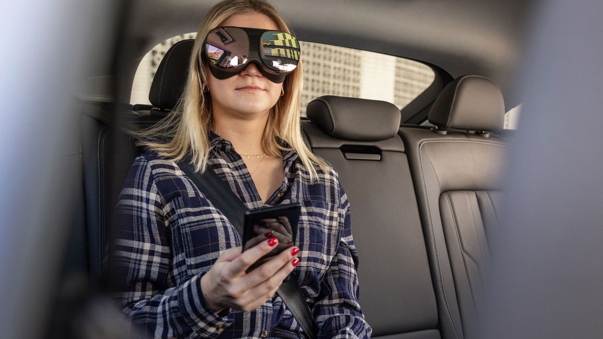 Una mujer, sentada en el asiento trasero de un vehículo, utiliza la tecnología holoride con unas gafas 3D.