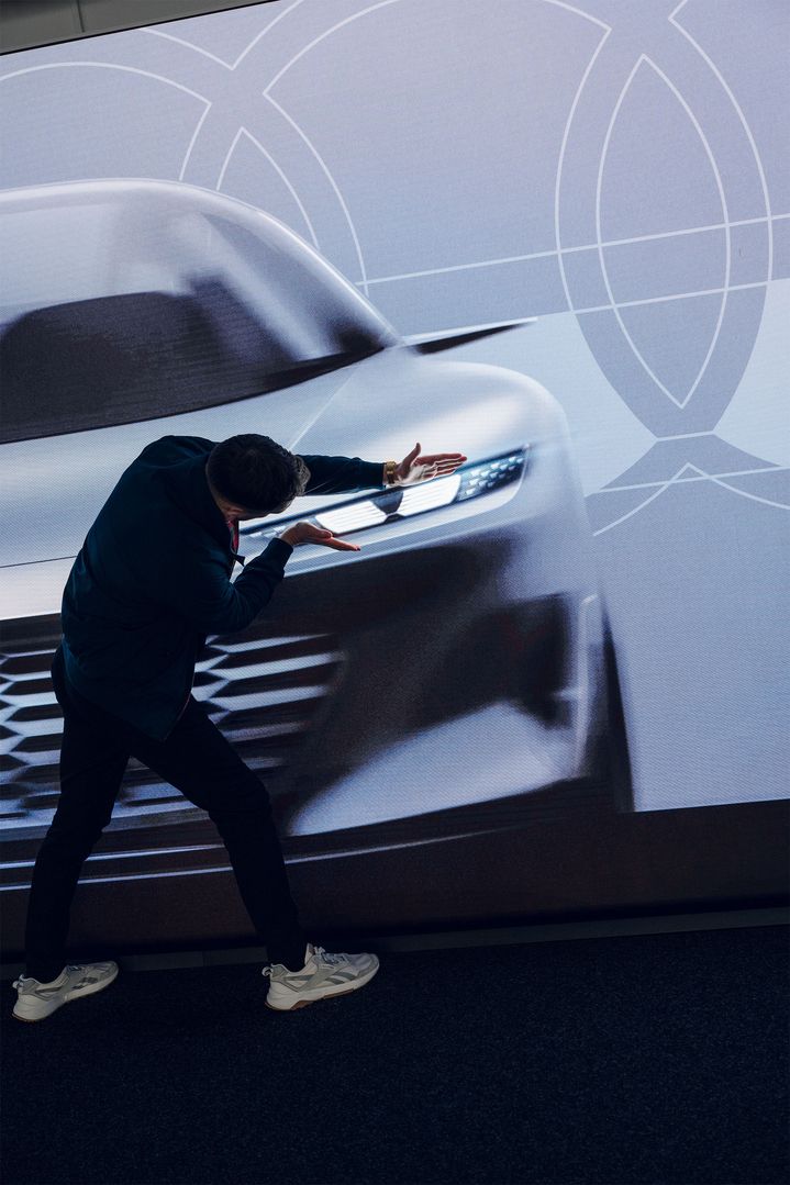 Le designer Lukas Rittwage fait des gestes devant la projection d'un véhicule.