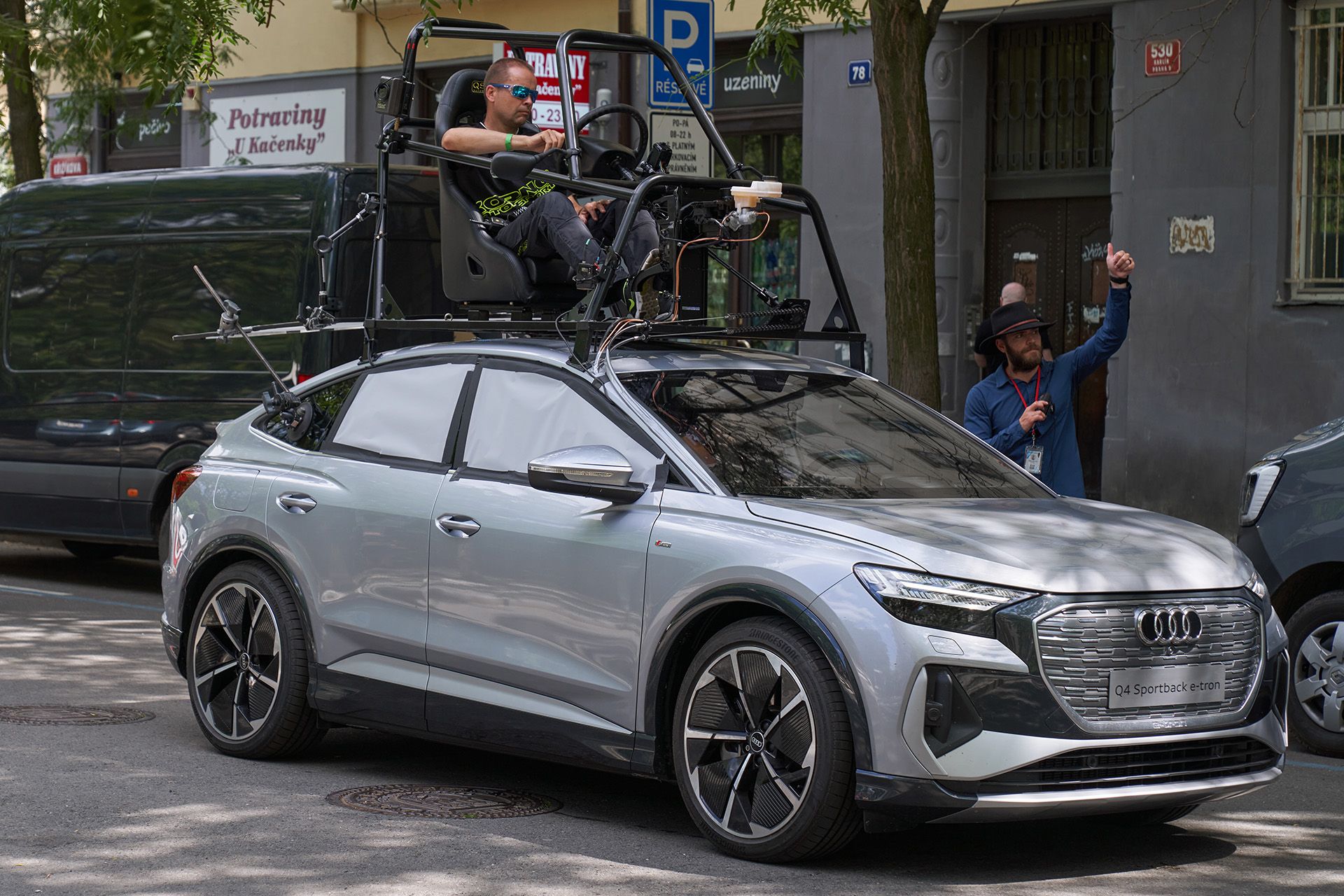 The Audi Q4 e-tron Sportback waits on set for the scene to be shot. A stunt driver can be seen sitting on the roof in the so-called pod car rig.