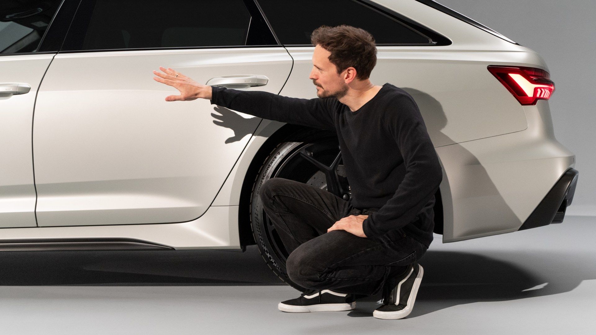 Markus Eberle crouching at the side of the Audi RS 6 Avant performance, pointing his hand to the rear door.