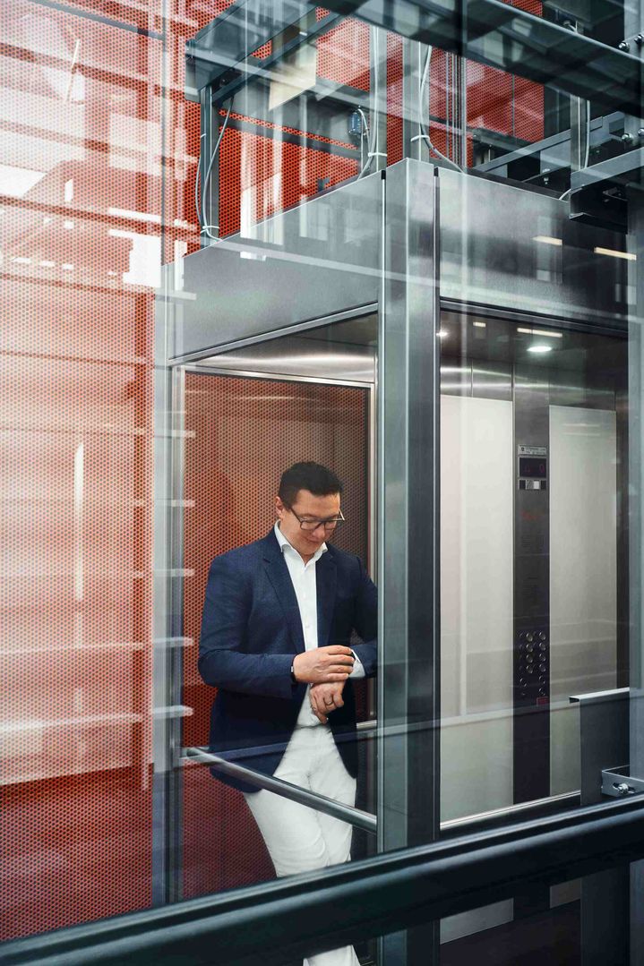 Giorgio Delucchi guarda il suo orologio all'interno di un ascensore di vetro.