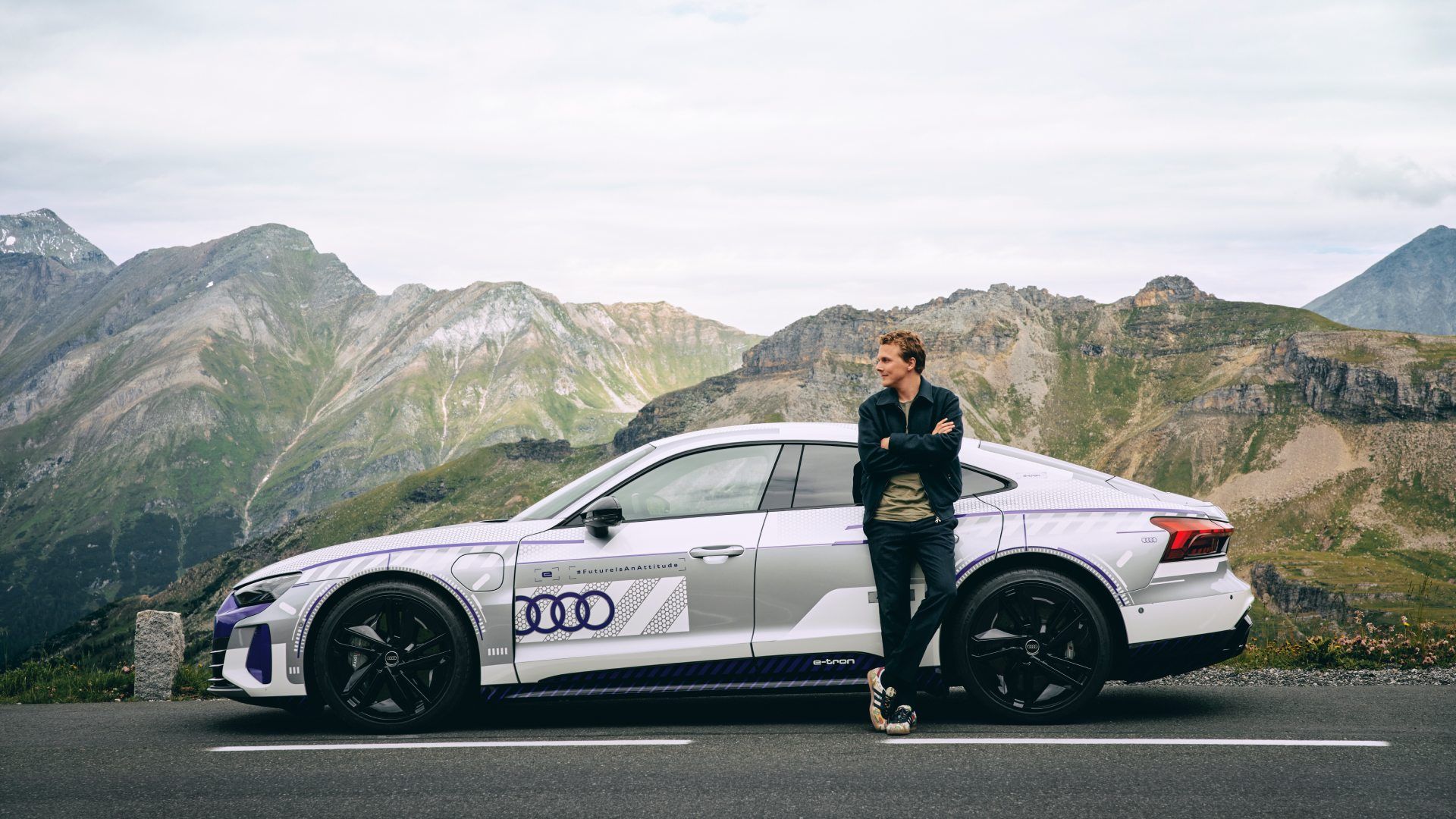 Ferdinand Porsche leaning on the Audi RS e-tron GT ice race edition. In the background is mountain scenery.